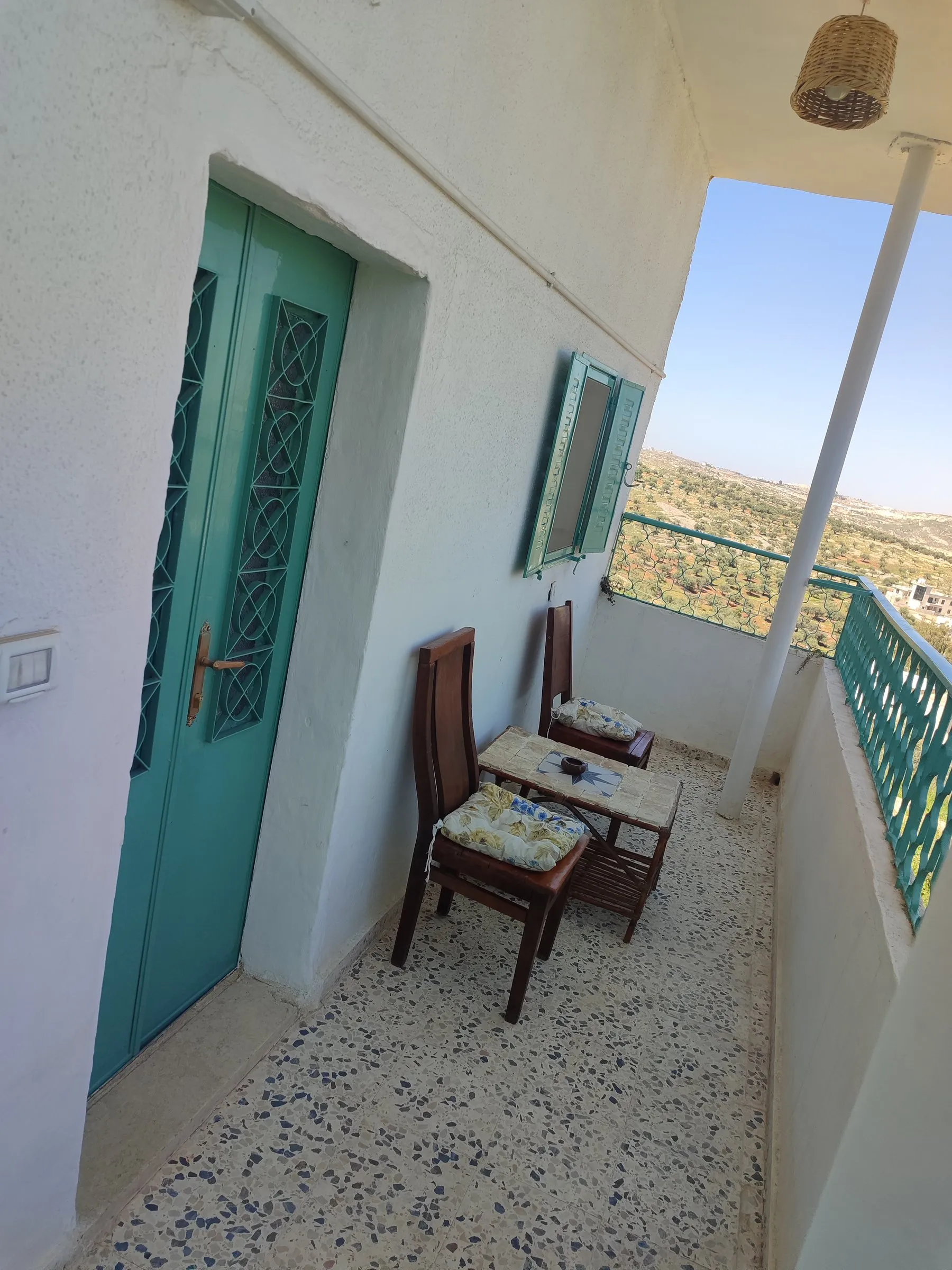 A teal door opening onto a balcony with chairs